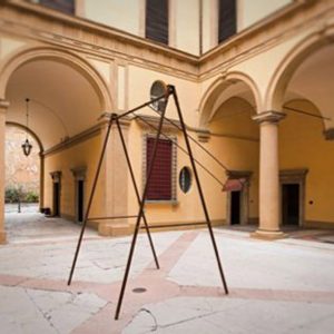 A modern sculpture consisting of an old iron swing with the seat still suspended in the air, installed in the middle of an ancient courtyard. Sculpture by Dado