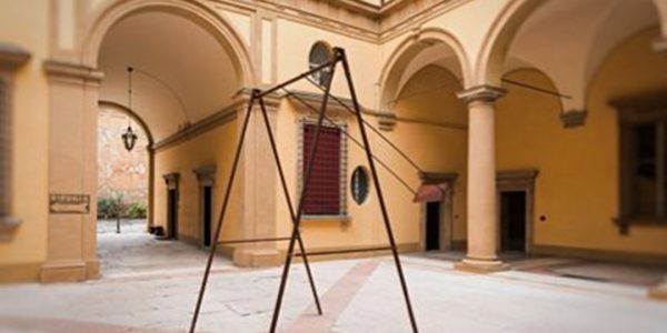 A modern sculpture consisting of an old iron swing with the seat still suspended in the air, installed in the middle of an ancient courtyard. Sculpture by Dado