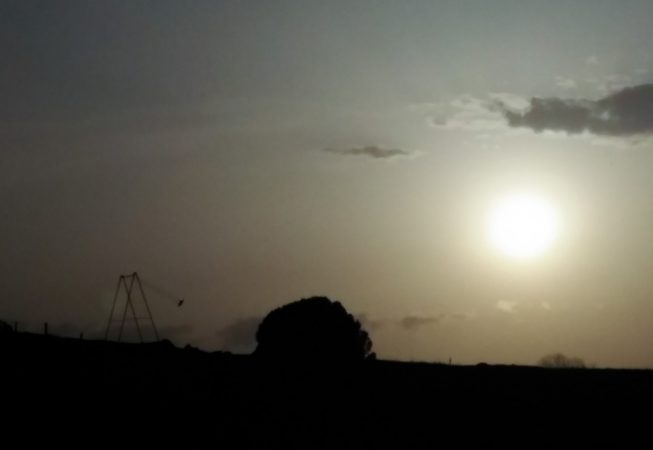 A sculpture installation consisting of an old iron swing with the seat still suspended in the air, at a long distance at the sunset. Sculpture by Dado