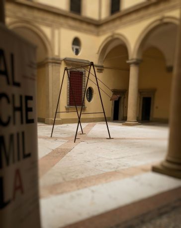A modern sculpture consisting of an old iron swing with the seat still suspended in the air, installed in the middle of an ancient courtyard . Sculpture by Dado