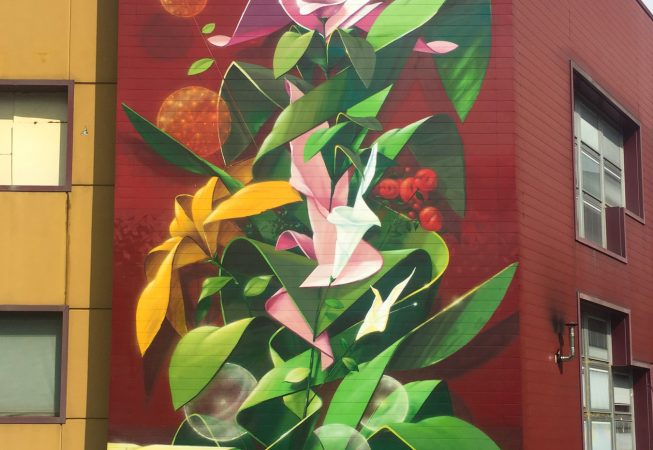 Total view of a big wall mural painting representing a ribbon wildstyle lettering various colored flowers spherical Dandelion seedheads and green leaves. Artwork by Dado.