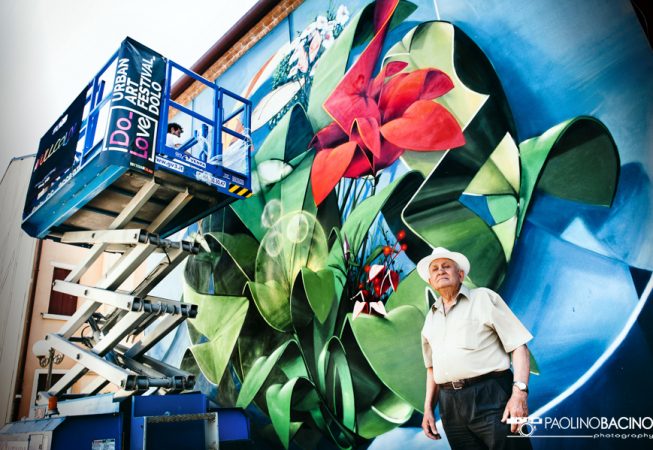 Dado painting a Graffiti-mural spherical lettering with multi colored flowers-bottom view of the entire wall and the artist on an industrial elevator