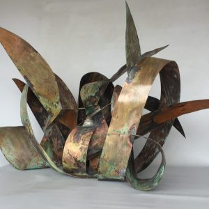 Front-lateral view of a copper sculpture made of sinous intricated ribbons forming the simbol of the infinite in mixed with natural elements. Artwork by Dado