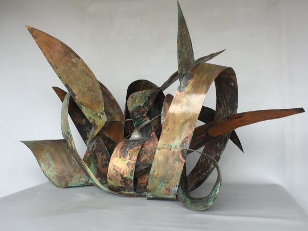 Front-lateral view of a copper sculpture made of sinous intricated ribbons forming the simbol of the infinite in mixed with natural elements. Artwork by Dado