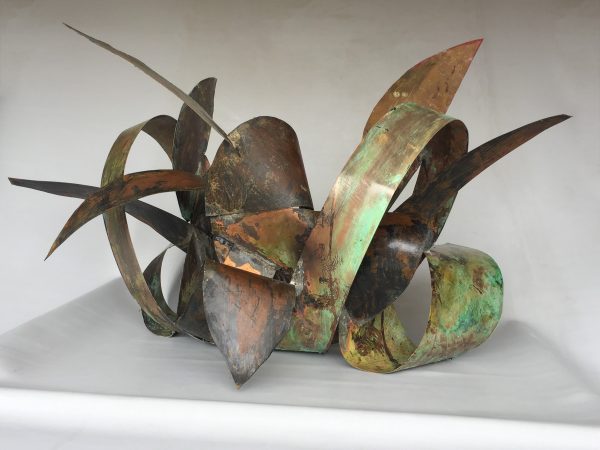 Back-lateral view of a copper sculpture made of sinous intricated ribbons forming the simbol of the infinite in mixed with natural elements. Artwork by Dado