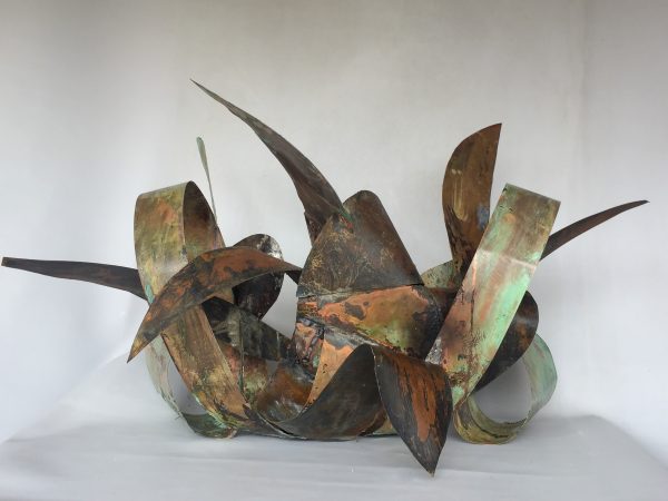 Back view of a copper sculpture made of sinous intricated ribbons forming the simbol of the infinite in mixed with natural elements. Artwork by Dado