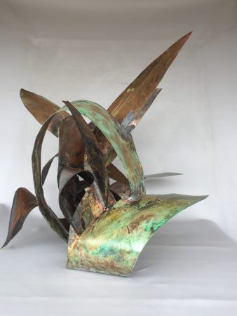 Side view of a copper sculpture made of sinous intricated ribbons forming the simbol of the infinite in mixed with natural elements. Artwork by Dado