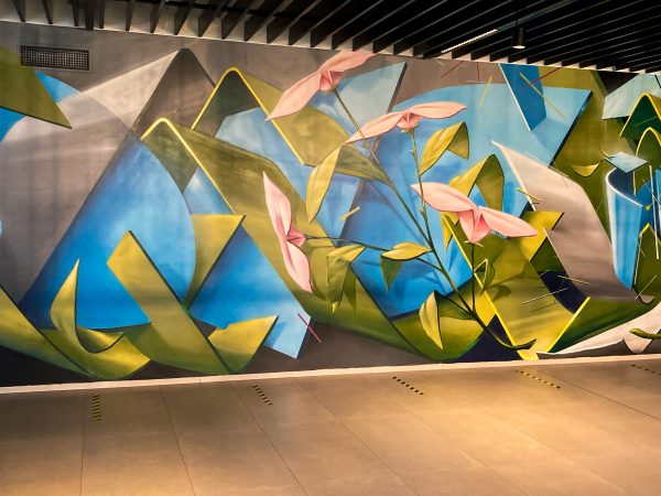 Detail of a wall decoration representing intersecting blue and green ribbons pattern and a bunch of pink flowers appearing on the right. Aerosol art by Dado.