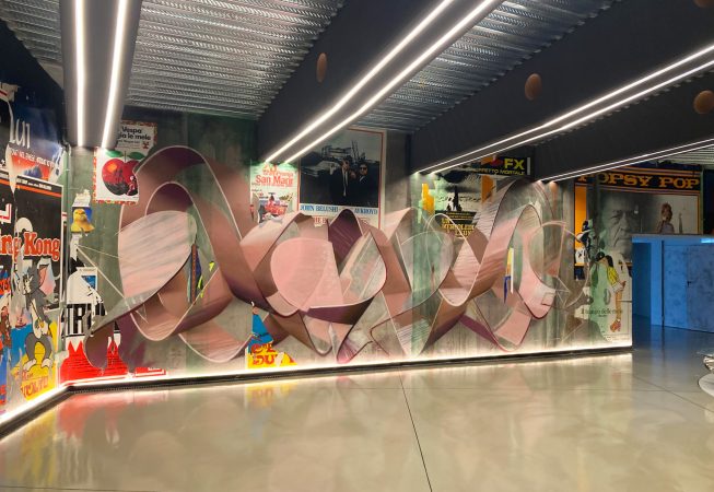 Total view of a decorated garage wall recreating a street underground atmospherewith spray can lettering artworks and torn paper posters. Artwork by Dado.