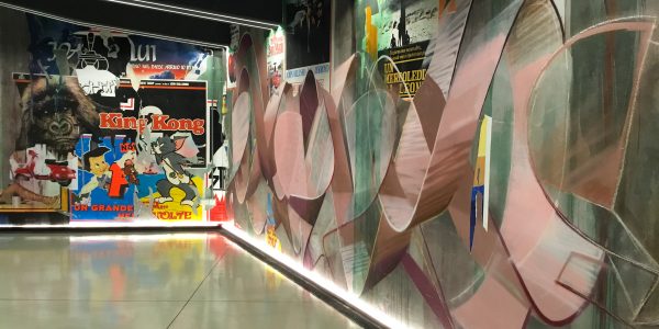Right total view of a decorated garage wall recreating a street underground atmosphere with spray can lettering artworks and torn paper posters. Artwork by Dado.