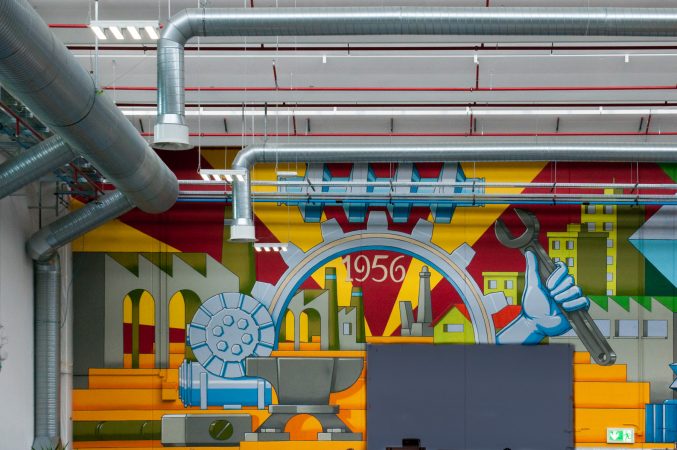 Detail of a big wall painting representing the company first logo in the factory warehouse interior. Wall painting by Dado.
