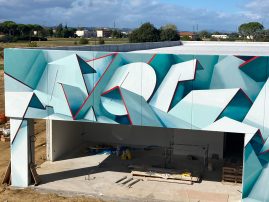 Closer front view of a graffiti paint work on the external walls of a big building representing flat ribbons bent in geometrical shapes, light blue and white shades with thin red outlines. Artwork by Dado