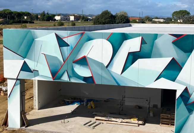 Closer front view of a graffiti paint work on the external walls of a big building representing flat ribbons bent in geometrical shapes, light blue and white shades with thin red outlines. Artwork by Dado