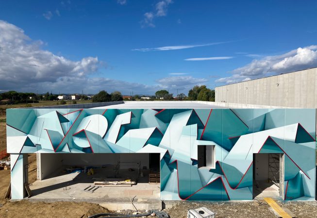 Total front view of a graffiti paint work on the external walls of a big building representing flat ribbons bent in geometrical shapes, light blue and white shades with thin red outlines. Artwork by Dado