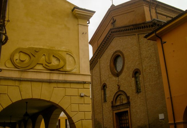 Bas-relief sculpture in a contemporary graffiti lettering fixed on a above a Medieval vault architecture. In the background an old Church. Artwork by Dado