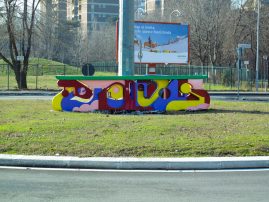 A graffiti style bright colored sculpture in the middle of a traffic circle in a public road path. Installation by Dado