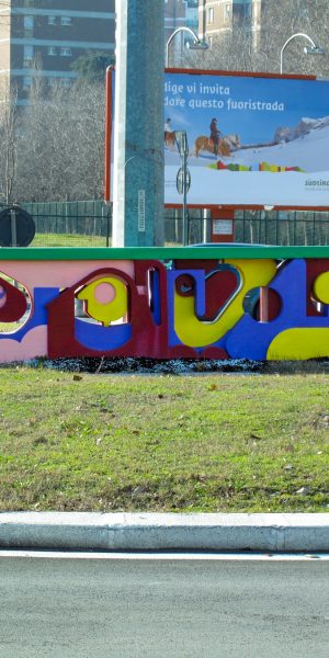 A graffiti style bright colored sculpture in the middle of a traffic circle in a public road path. Installation by Dado
