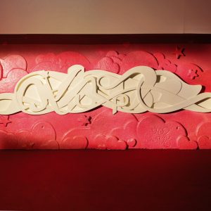 Bas-relief sculpture in a contemporary graffiti lettering plain white on pink hearted background. Front wide view Artwork by Dado