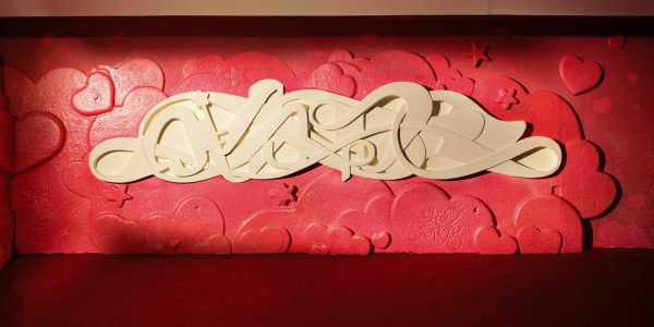 Bas-relief sculpture in a contemporary graffiti lettering plain white on pink hearted background. Front wide view Artwork by Dado
