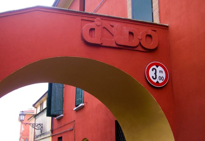 Bas-relief sculpture in a contemporary graffiti lettering fixed on a above a Medieval bridge red architecture. Front view Artwork by Dado
