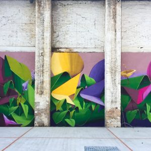 A triptych mural painting of flowers in three different colors on a white bricks wall in a wide open space, total view. Artwork by Dado
