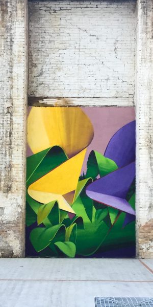 A triptych mural painting of flowers in three different colors on a white bricks wall in a wide open space, total view. Artwork by Dado
