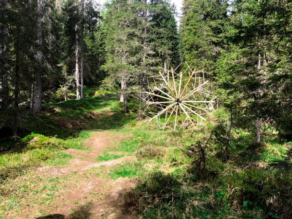 A big wood sculpture, seems to rolling out the forest, composed of clear wood sticks joined together to form a geometrical spherical structure resembling a dandelion. Artwork by Dado