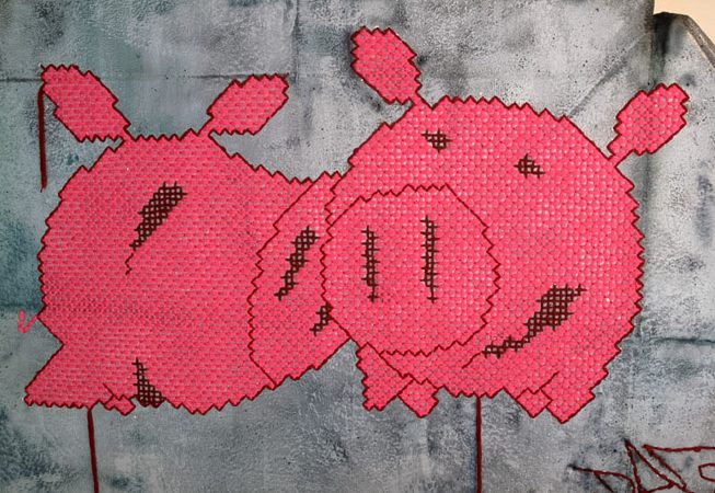 A closeup detail of two wool made flat pig characters stitched on a big rock sculpture. Artwork by Dado