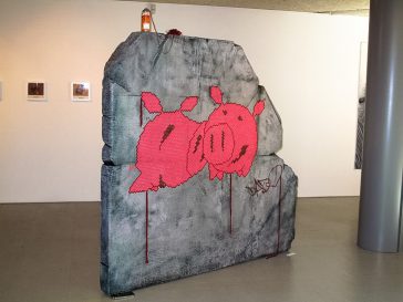 A big rock sculpture with two wool made flat pig characters stitched in the middle. Artwork by Dado