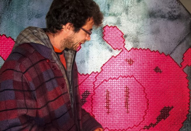 The artist Dado closely watching one pig face character made of wool stitched on his own rock sculpture.