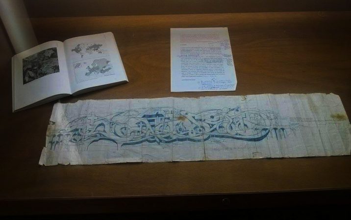Blue crayon graffiti sketch on white paper depicting the tag Dado in an elaborated 3D lettering style, decorated with graphical elements like crosses and arcs