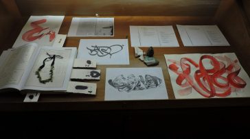 A museum showcase displaying various drawings and sketches by Dado Ferri