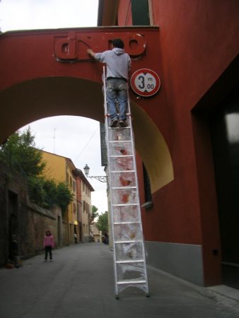 The artist Dado Ferri on a work ladder applying the bas-relief Sculpture named Soprail Ponte on a wall for the Exhibition