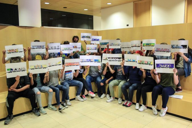 A big group of kids sitting on benches disposed on three layers, every kid is displaying a paper sheet in front of his face to show his own drawing