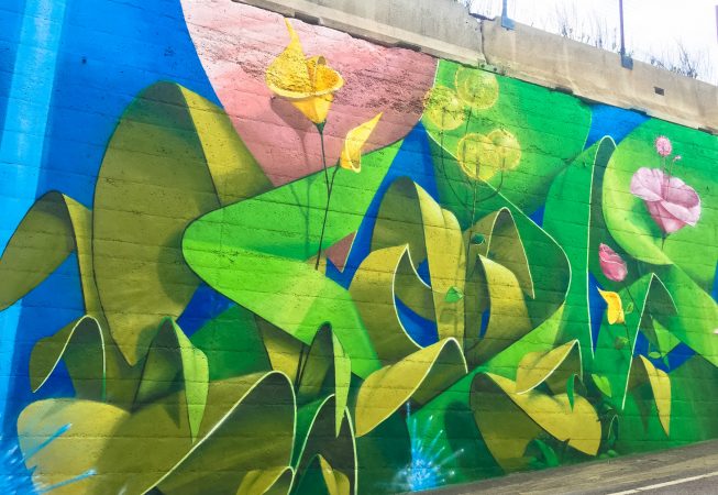 Lateral view of a Mural Painting depicting the name of the city Covignano woven with colored flowers and green leaves. Artwork by Dado