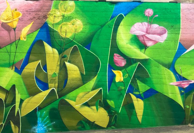 Detail of green leaves and pink flowers on a Mural Painting depicting the name of the city Covignano woven with colored flowers and green leaves. Artwork by Dado