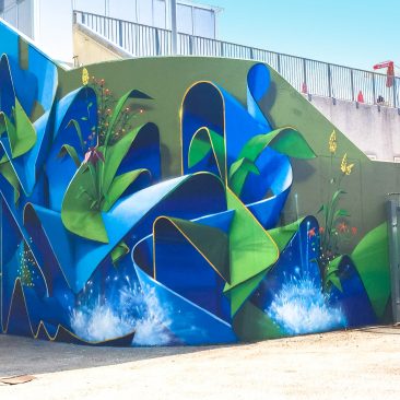 Total view of a large mural painting depicting wide sinuous blue ribbons decorated with purple, red and yellow flowers and green leaves and water splashes. Artwork by Dado