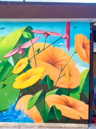 Detail of a mural painting depicting big yellow-orange flowers and smaller pink and light yellow flowers floating on deep blue water. Artwork by Dado
