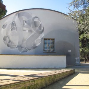 Wide view of a mural painting depicting a spherical wildstyle graffiti forming the tag Dado colored in a very vanishing white and light gray tones.