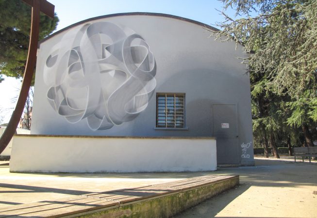 Wide view of a mural painting depicting a spherical wildstyle graffiti forming the tag Dado colored in a very vanishing white and light gray tones.