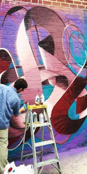 The artist Dado Ferri painting a Mural Artwork of his own tag in a spherical shape on a brick wall in New York