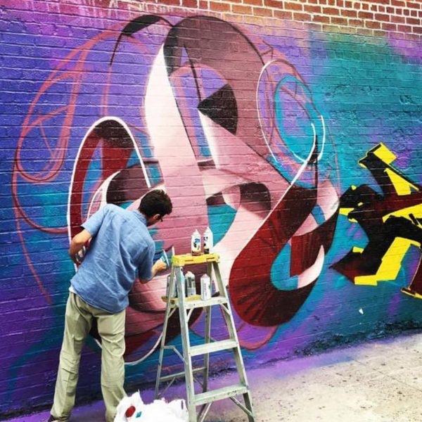 The artist Dado Ferri painting a Mural Artwork of his own tag in a spherical shape on a brick wall in New York