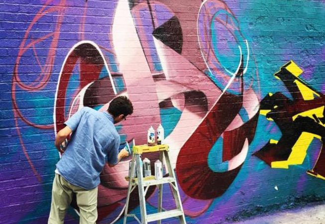 The artist Dado Ferri painting a Mural Artwork of his own tag in a spherical shape on a brick wall in New York