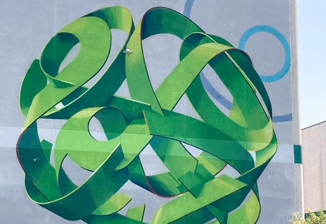 Total view of a mural painting depicting a spherical wildstyle graffiti forming the tag Dado in green tones.