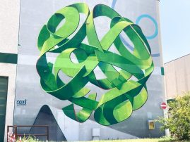 Total view of a mural painting depicting a spherical wildstyle graffiti forming the tag Dado in green tones.