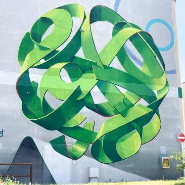 Total view of a mural painting depicting a spherical wildstyle graffiti forming the tag Dado in green tones.