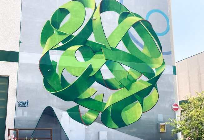 Total view of a mural painting depicting a spherical wildstyle graffiti forming the tag Dado in green tones.
