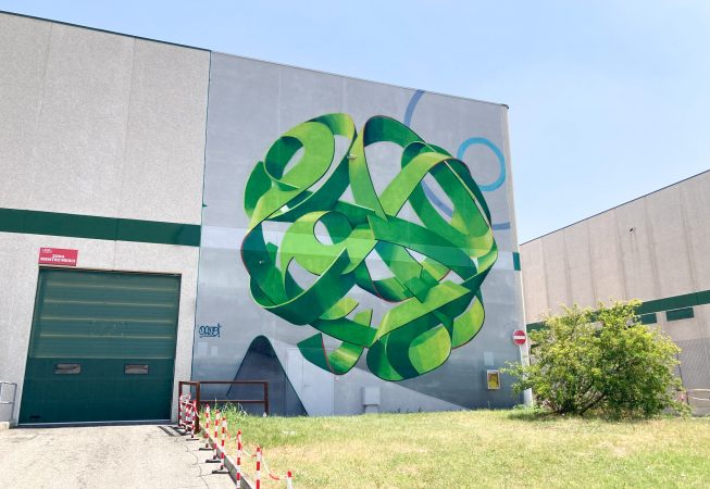 Wide location view of a mural painting depicting a spherical wildstyle graffiti forming the tag Dado in green tones.
