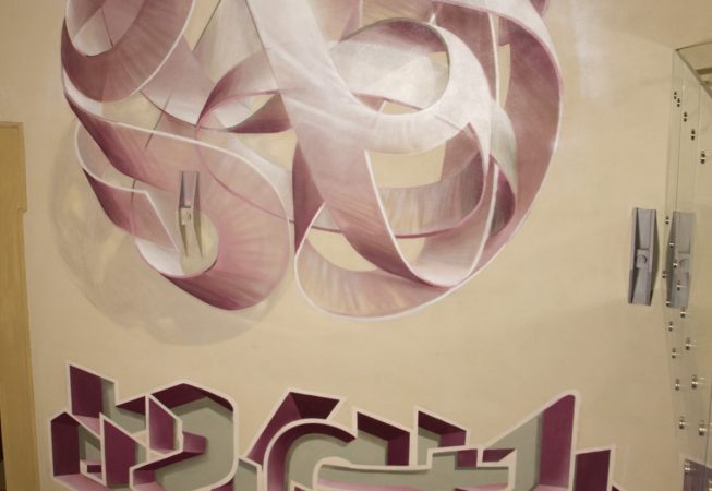 Protrait view of a mural painting on an indoor wall depicting a spherical wildstyle graffiti forming the tag Dado colored in a vanishing light pink and winy tones along with another lettering graffiti underneath it.