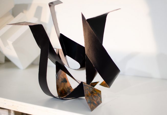 Back view of a sculpture made of copper ribbons forming M and G letters. Artwork by Dado